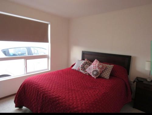 a bedroom with a bed with a red comforter and a window at Greyhouse in Puerto Natales