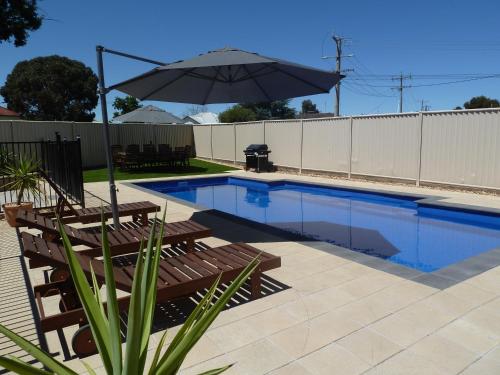 a swimming pool with benches and an umbrella at Ploughmans Motor Inn in Horsham