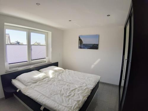 1 dormitorio con 1 cama con sábanas blancas y 2 ventanas en Wellenreiter 1, en Breege