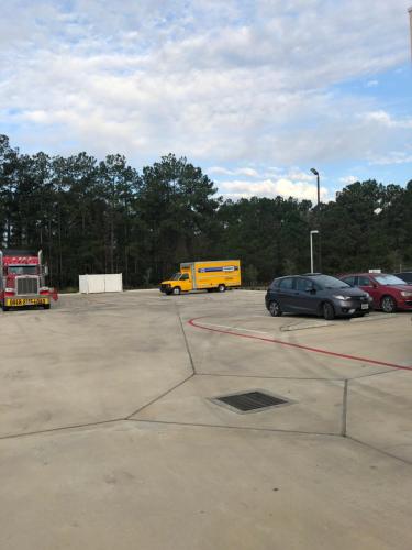 a parking lot with cars and a yellow truck at Baymont by Wyndham Kingwood in Kingwood