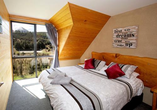 Un dormitorio con una cama grande con almohadas rojas y una ventana en Mt Lyford Holiday Homes, en Mt Lyford