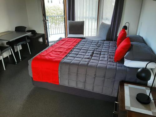 a bedroom with a bed with a red and gray comforter at Bayside Motel Whitianga in Whitianga