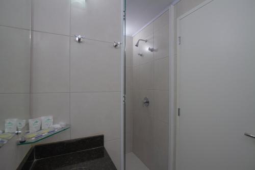 a shower with a glass door next to a sink at Hotel Confiance Barigui in Curitiba