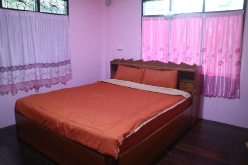 a bedroom with a bed with orange sheets and pink curtains at Baanmakpoo บ้านหมากพลู in Sangkhla Buri