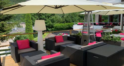 a patio with chairs and an umbrella on a deck at Hotel Le Panorama in Le Mont-Dore