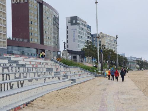 a group of people walking on a beach with buildings at Hotel Wooyeon Flora in Boryeong