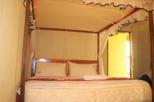 a canopy bed with white pillows in a bedroom at Pride Travellers Hotel Mubende in Mubende