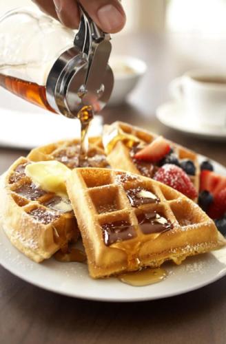 une personne verse du sirop sur une assiette de gaufres dans l'établissement Country Inn & Suites by Radisson, Oklahoma City - Bricktown, OK, à Oklahoma City