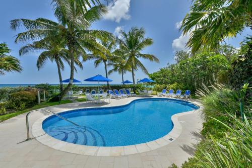 uma piscina com cadeiras e guarda-sóis azuis em Maxwell Beach Villas em Christ Church