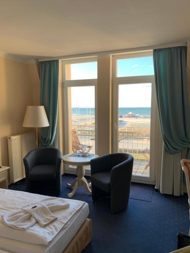 a hotel room with a bed, chair, table and window at Hotel Bellevue Warnemünde in Warnemünde