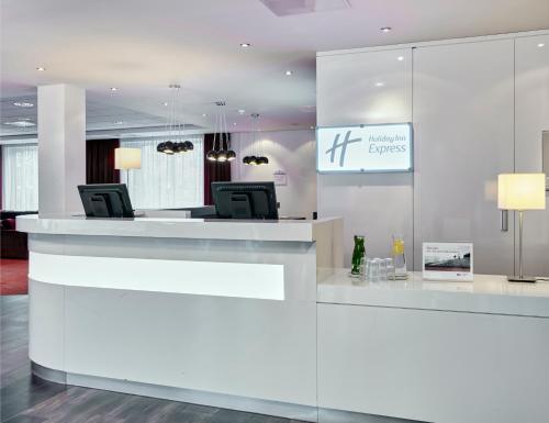 a white lobby with a reception desk with chairs at Holiday Inn Express Amsterdam - Schiphol, an IHG Hotel in Hoofddorp