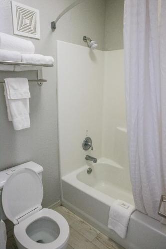 a bathroom with a toilet and a bathtub with a shower curtain at Mockingbird Inn & Suites in Monroeville