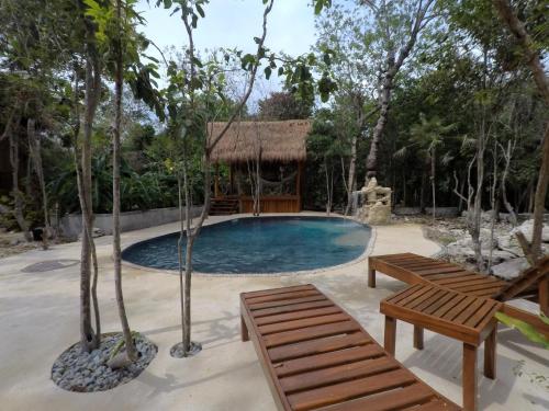 a swimming pool with two benches and a hut at Tulum Nueve in Tulum
