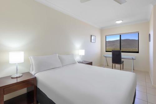 a bedroom with a white bed and a desk and a window at Piermonde Apartments Cairns in Cairns