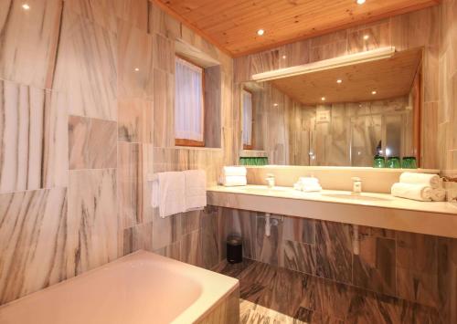 bagno con vasca, lavandino e specchio di Kia Ora Hotel Restaurant a Wagrain
