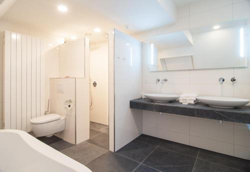een witte badkamer met 2 wastafels en een toilet bij Herberg Erve Kots Logement in Lievelde