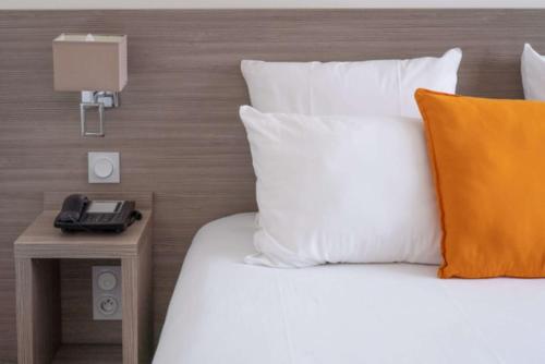 a bed with white pillows and a phone on a table at Best Western Hôtel des Thermes - Balaruc les Bains Sète in Balaruc-les-Bains