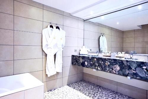 La salle de bains est pourvue de peignoirs blancs accrochés au mur. dans l'établissement Golden Tulip Bâle Mulhouse - Hôtel Restaurant, à Sausheim