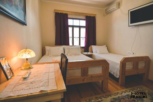 a room with two beds and a table and a desk at Hotel Brahimi in Gjirokastër