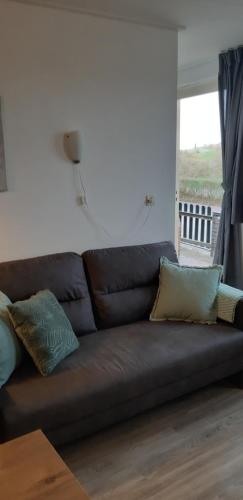 ein braunes Sofa mit Kissen im Wohnzimmer in der Unterkunft Bij De Vuurtoren in Hollum