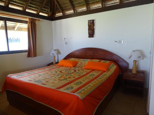 a bedroom with a bed with an orange comforter and two lamps at Hôtel Atiapiti in Opoa