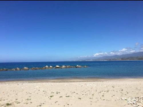 a beach with blue water and rocks in the distance at Residence Baia Blu Falcone in Falcone