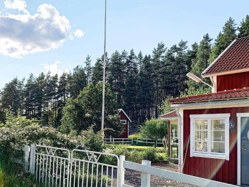 une maison rouge avec une clôture blanche devant une forêt dans l'établissement 5 person holiday home in GAMLEBY, à Karrum