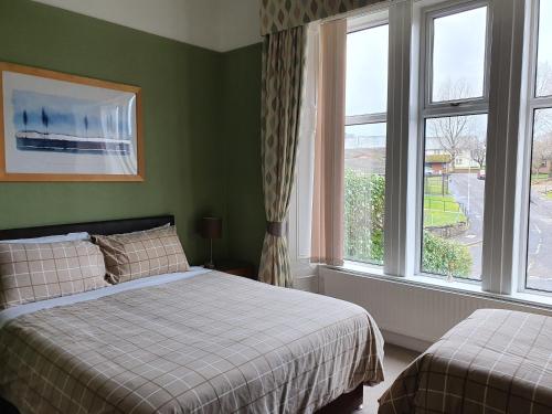 a bedroom with two beds and two windows at Dean Park Guest House in Kilmarnock