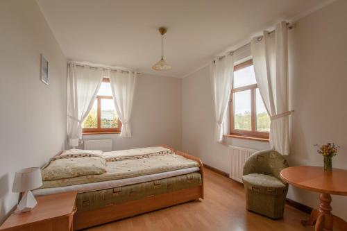 a bedroom with a bed and a table and two windows at Dom Gościnny na Górce in Leszczewek