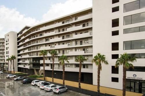 a large white building with palm trees in front of it at Waters Edge Apartments in Cape Town