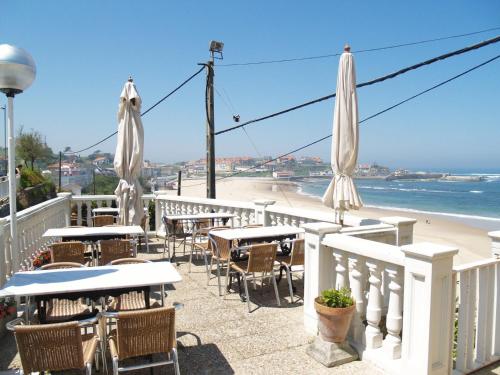 a patio with tables and umbrellas and the beach at Hotel Josein in Comillas