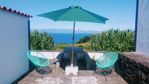a table and chairs with an umbrella and the ocean at Casa do Paim in São Roque do Pico