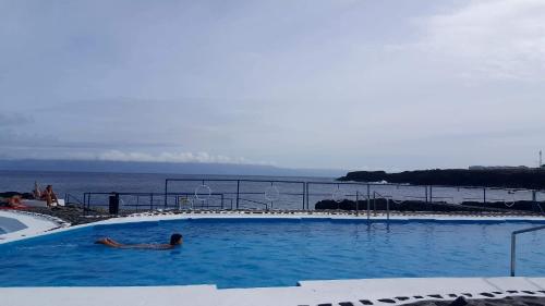 a person laying in a swimming pool next to the ocean at Casa do Paim in São Roque do Pico