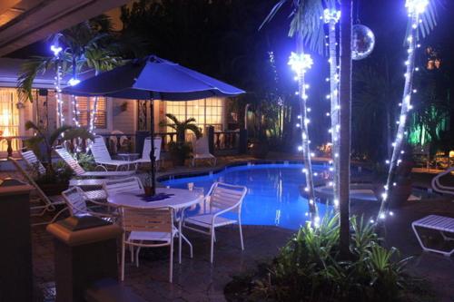 a patio with a table and chairs and a pool at night at Coral Reef Guesthouse in Fort Lauderdale