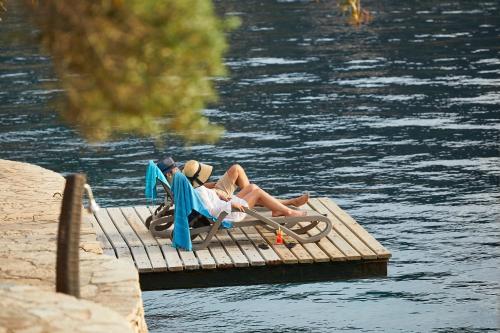 
two people sitting on a wooden bench next to a body of water at Hotel Villa Mahal in Kalkan
