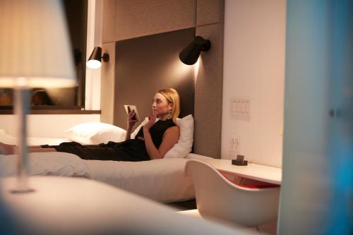 a woman sitting on a bed reading a book at citizenM Paris Charles de Gaulle Airport in Roissy-en-France