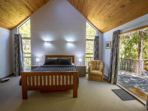 a bedroom with a bed and a chair and windows at Kanuka House - Kaiteriteri Holiday Home in Kaiteriteri