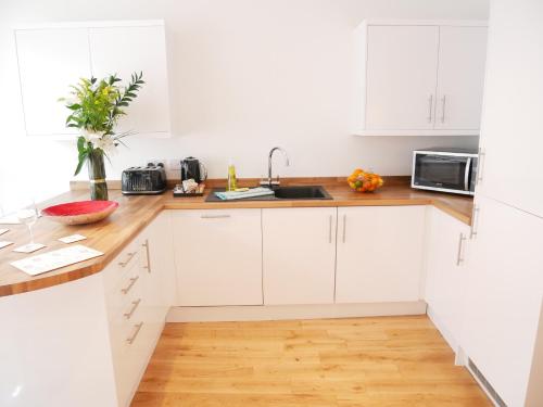a white kitchen with white cabinets and a wooden floor at The Courtyard, 4 - Bed, Sleeps 6, Pets Welcome in Ulverston