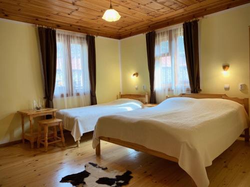 a bedroom with two beds and two tables and windows at Bobi Guest House in Koprivshtitsa