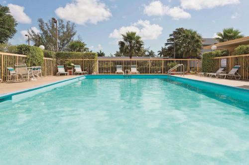 a large swimming pool with chairs and a fence at La Quinta Inn by Wyndham West Palm Beach - Florida Turnpike in West Palm Beach