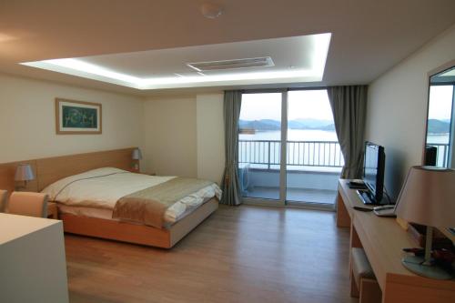 a bedroom with a bed and a television and a balcony at Kumho Tongyeong Marina Resort in Tongyeong