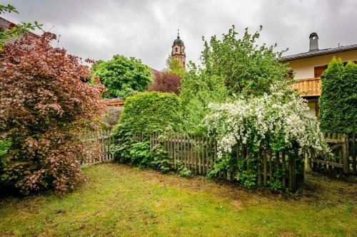 a garden with a fence and trees and a clock tower at Hoglhaus & Malerwinkel in Mittenwald