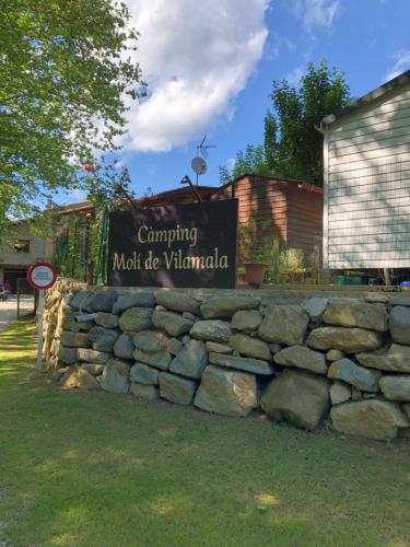 a sign on a stone wall in front of a building at Càmping Molí de Vilamala in Les Planes d'Hostoles
