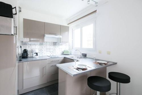 uma cozinha com armários brancos e bancos pretos em Studio neuf proche Disneyland Paris em Meaux
