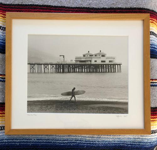 a picture of a man walking on the beach with a surfboard at The M Malibu in Malibu