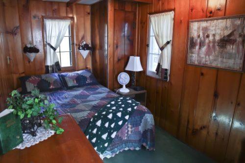 a bedroom with a bed and a table and windows at Cabin #1 - Cedar Village cabin in Carp Lake
