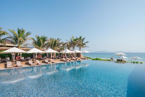 a swimming pool with chairs and umbrellas and the ocean at Fusion Resort Cam Ranh - All Spa Inclusive in Cam Ranh