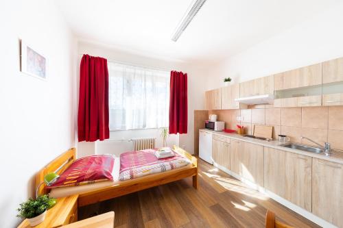 a room with a bed and a kitchen with red curtains at Penziony Beneš in Prague