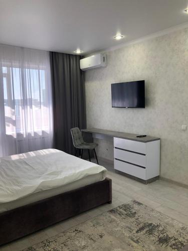 Schlafzimmer mit einem Bett, einem Schreibtisch und einem TV in der Unterkunft Новая современная квартира в центре города in Qostanai