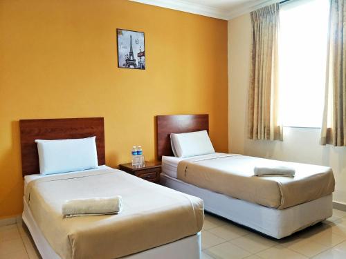 two beds in a hotel room with yellow walls at Tropicana Hotel in Gemas